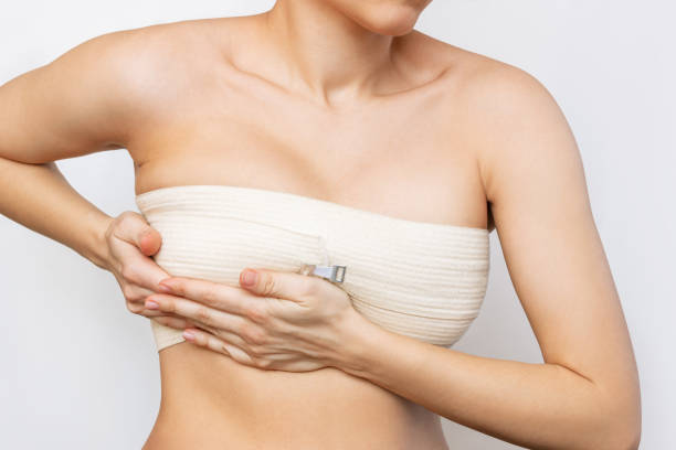 Cropped shot of young woman with elastic bandage after breast augmentation with silicone implants isolated on white background.The result of lifting. Breast size correction. Pain after plastic surgery